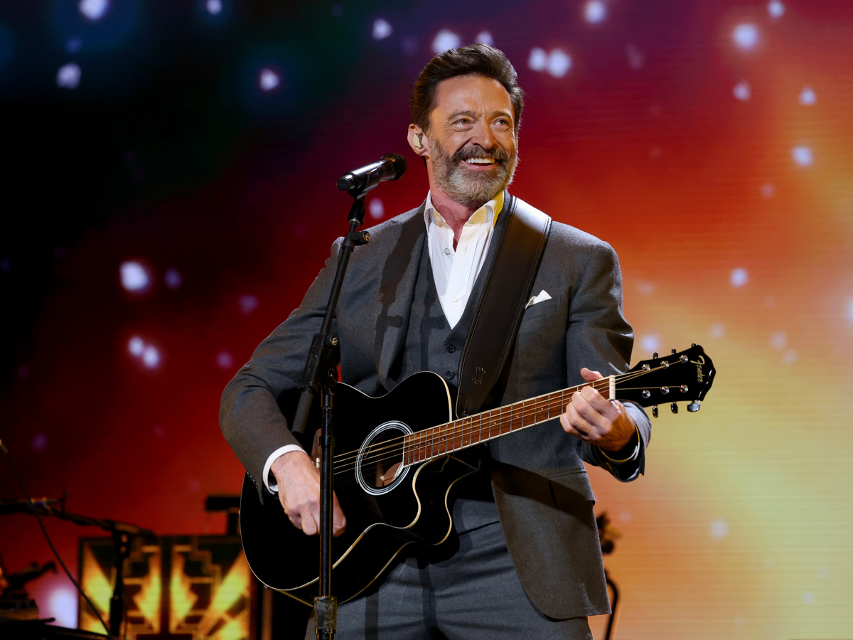 Hugh Jackman holds a guitar and smiles